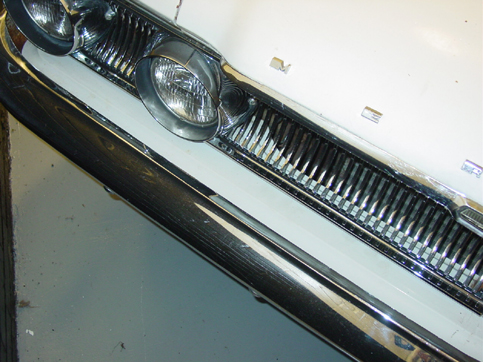 Close-up of vintage car front grille, dual round headlights, and chrome bumper on white body