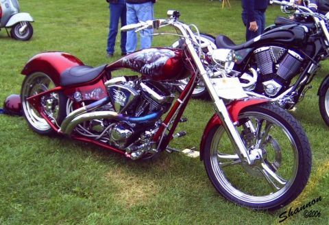 1982 Ford Bronco - A custom motorcycle with intricate artwork sits on display next to another bike and a scooter.