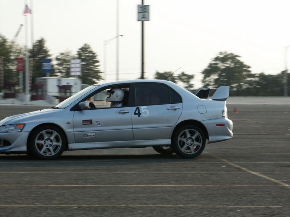 Silver sedan with racing number 45 on the door, a driver in a helmet, and a large rear spoiler, seen from the side