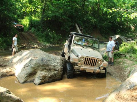 1996 Ford Bronco - Two Jeeps tackle an off-road trail with water and large rocks.