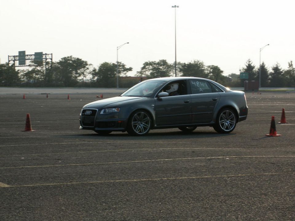 Dark gray sedan with racing cones on a track, driver wearing a helmet