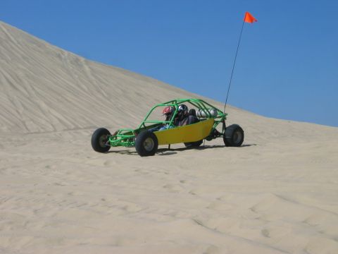 1985 Ford Bronco - Dune buggy with two occupants navigates a sandy terrain under a clear blue sky.