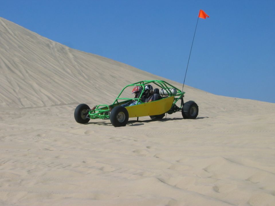 Green-frame yellow dune buggy with orange flag on a sand dune