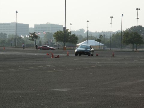 2001 Mercury Grand Marquis - A black sedan navigates a course marked by orange cones on a hazy day, with a red sports car visible in the distance.