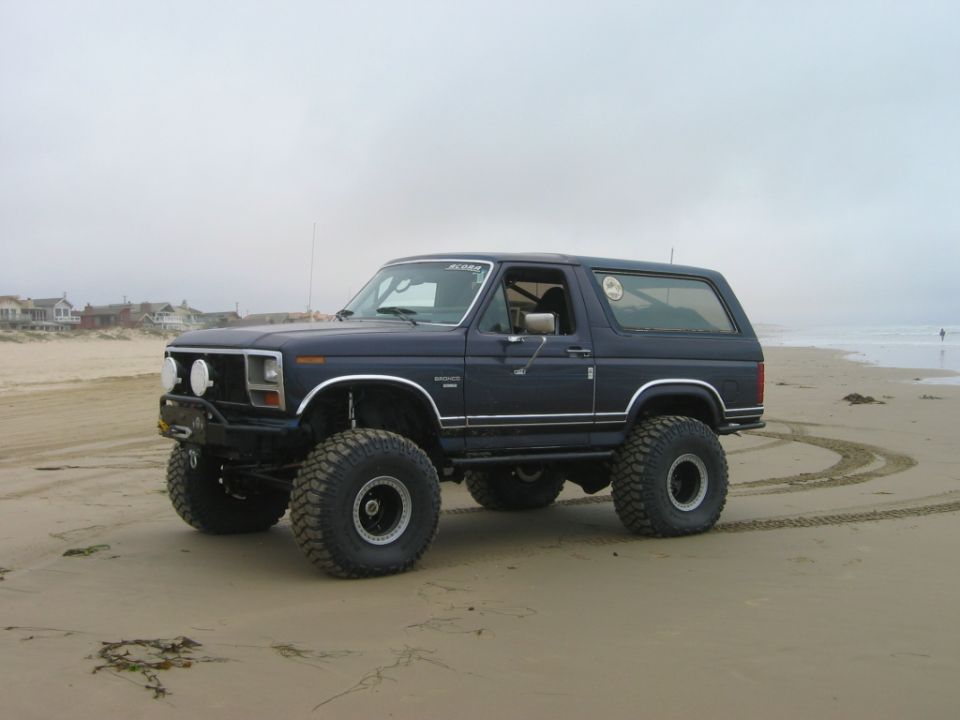 Dark blue lifted Ford Bronco SUV on a beach with large off-road tires