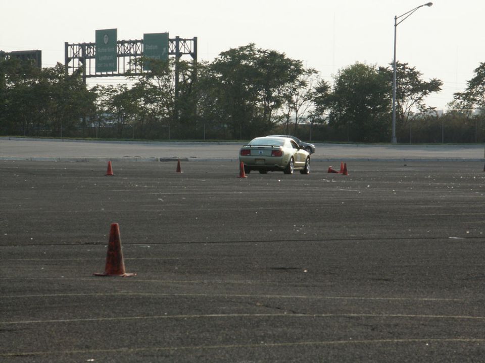 Gold Ford Mustang driving on a track with cones. Highway signs in background