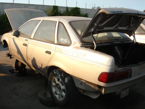 1993 Ford Taurus - A silver 1992 Ford Taurus sedan sits in a junkyard with its hood and trunk open, missing its front wheels.
