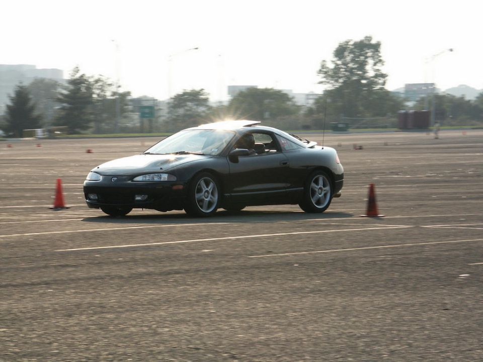 Black coupe on track, front 3/4 view. Supermotors.net logo visible