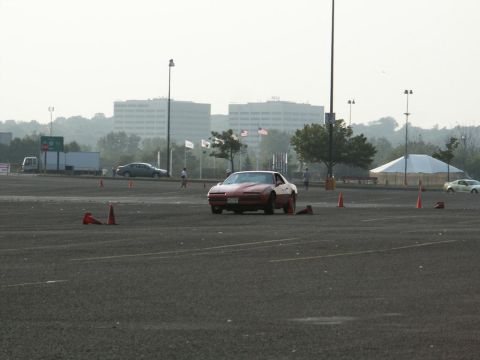 2001 Mercury Grand Marquis - A red sports car navigates a course marked by orange cones, with buildings and a tent in the background.