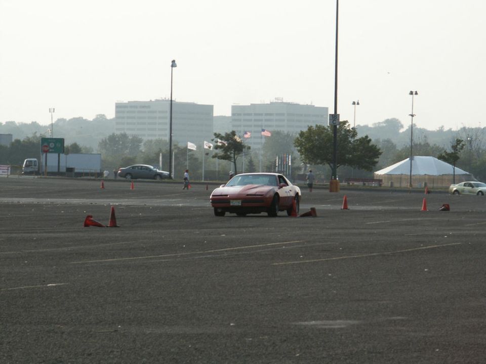 Red sports car with a white hood stripe, viewed from the front at an autocross event with orange cones