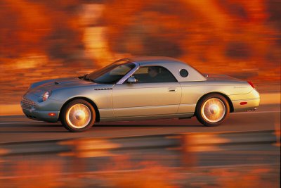 2002 Ford Thunderbird - A silver 2002 Ford Thunderbird convertible is captured in motion on a highway during sunset.