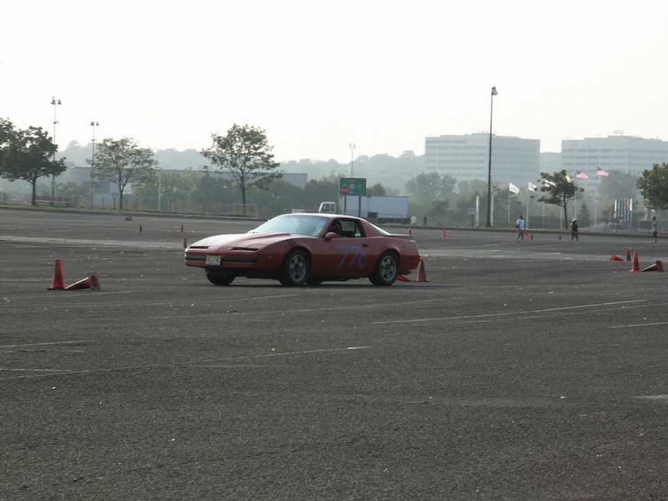 Red sports car with purple markings on the side, parked on asphalt with orange cones