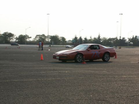 2001 Mercury Grand Marquis - A red sports car with blue racing numbers is parked on an asphalt lot, surrounded by orange cones.