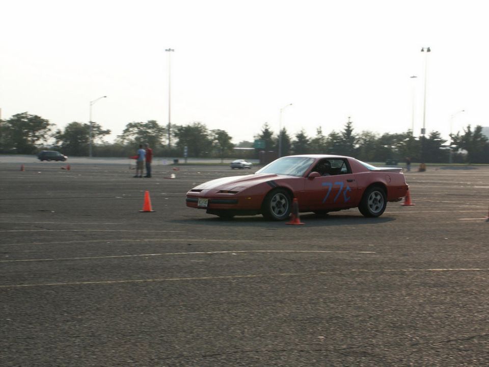 Red sports car with blue racing numbers on side, parked on asphalt with cones