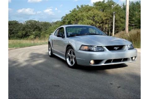 1998 Ford Taurus - A silver Ford Mustang is parked on the side of a road with trees in the background.