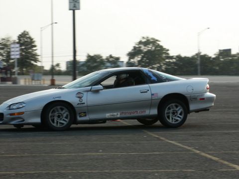 2001 Mercury Grand Marquis - A silver Chevrolet Camaro Z28 is seen from the side, driving on a paved surface with trees in the background.