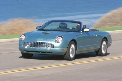 2002 Ford Thunderbird - A blue 2002 Ford Thunderbird convertible is captured in motion on a coastal highway.