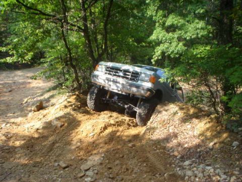 1987 Ford Bronco - A white 1987 Ford Bronco navigates a steep, muddy incline on a wooded trail.