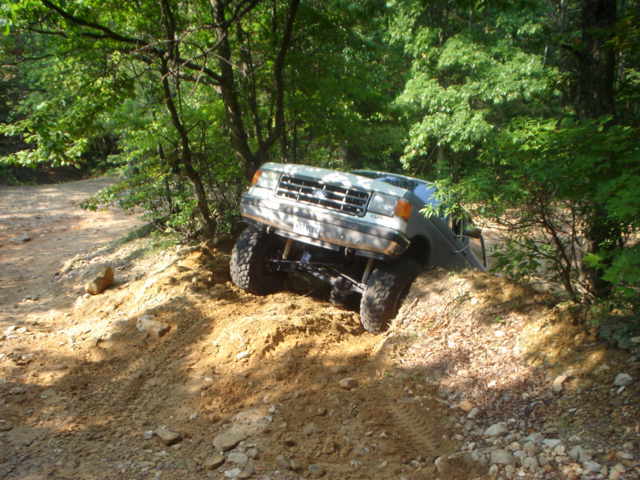 White 1987 Ford Bronco climbing a dirt hill, front 3/4 view, off-road tires