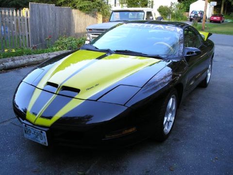 1994 Pontiac Trans Am - A black 1994 Pontiac Trans Am with yellow racing stripes and hood scoops is parked in a driveway.