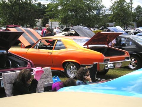 1994 Pontiac Trans Am - An orange muscle car with racing stripes is parked at an outdoor event, with other vehicles visible in the background.