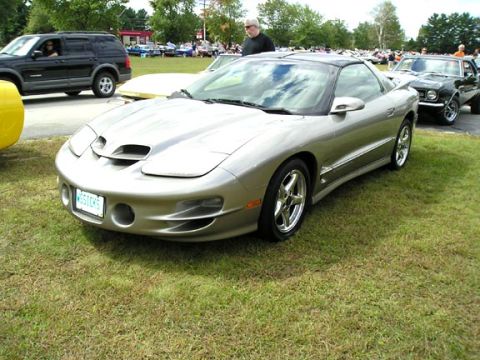 1994 Pontiac Trans Am - A silver 1994 Pontiac Trans Am is parked on a grassy area, with other vehicles visible in the background.