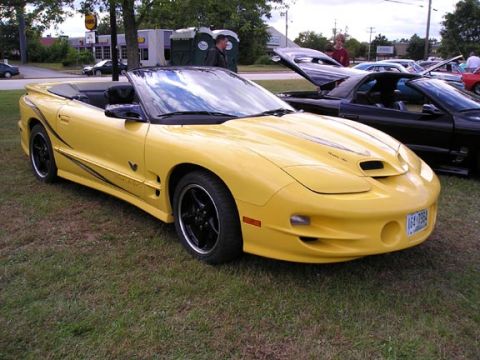 1994 Pontiac Trans Am - A yellow convertible sports car is parked on grass next to other vehicles.
