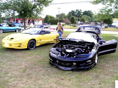1994 Pontiac Trans Am - Two Pontiac Firebirds are parked on grass, one black with its hood and doors open, the other yellow.