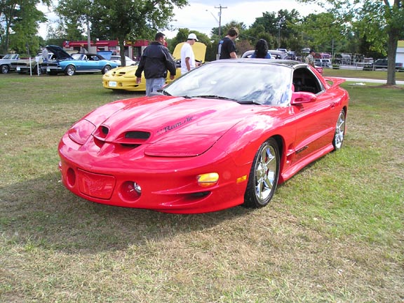 Red Pontiac Firebird parked on grass with other cars in background