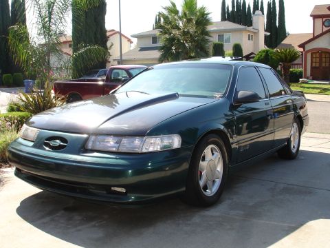 1993 Ford Taurus - A dark green sedan with a hood scoop and aftermarket wheels is parked in a suburban driveway.