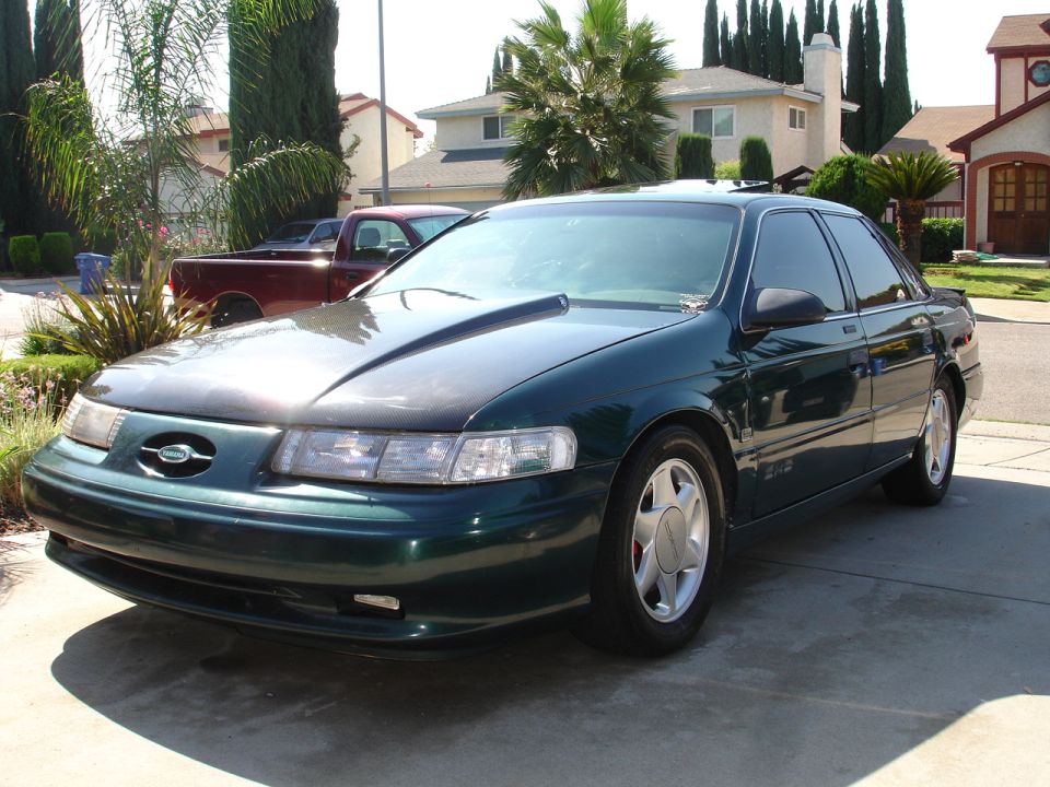 Green sedan with a hood scoop and aftermarket wheels parked on a driveway