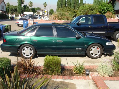 1993 Ford Taurus - A green 1993 Ford Taurus sedan is parked in a driveway next to a blue pickup truck.