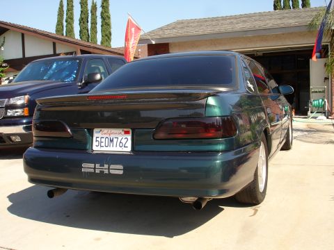 1993 Ford Taurus - The rear of a 1993 Ford Taurus SHO is visible, parked in a driveway next to a pickup truck.