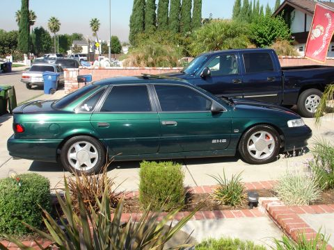 1993 Ford Taurus - A green 1993 Ford Taurus sedan is parked in a driveway next to a blue pickup truck.