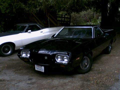 1972 Ford Ranchero - Two coupe utility vehicles are parked outdoors. The black one in the foreground has wire wheels and a hood scoop.