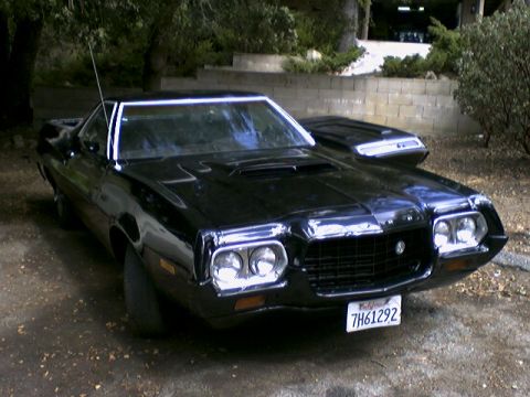 1972 Ford Ranchero - A black 1972 Ford Ranchero is viewed from a three-quarter front angle, showing its distinctive grille and hood.