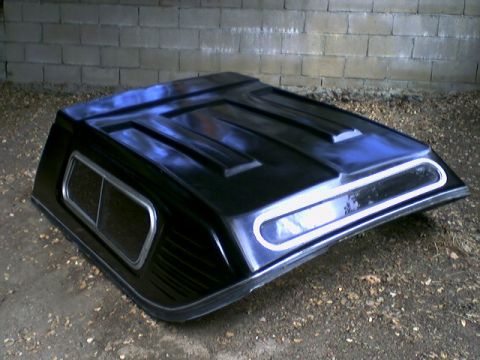 1972 Ford Ranchero - Black fiberglass truck bed cover with side window and louvered nose, sitting on the ground against a cinderblock wall.