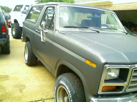 1985 Ford Bronco - A matte gray Ford Bronco is parked next to other vehicles, viewed from the front quarter.