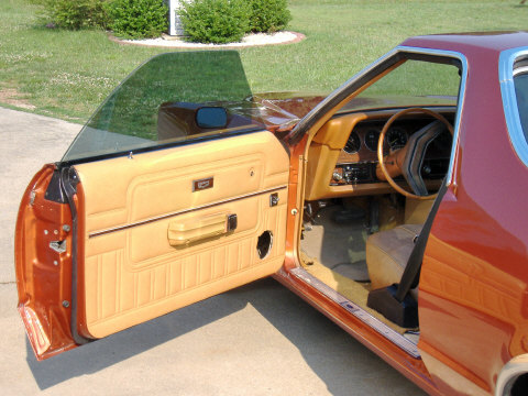 1979 Ford Ranchero - The interior of an orange pickup truck shows tan upholstery and a dashboard with a prominent steering wheel.