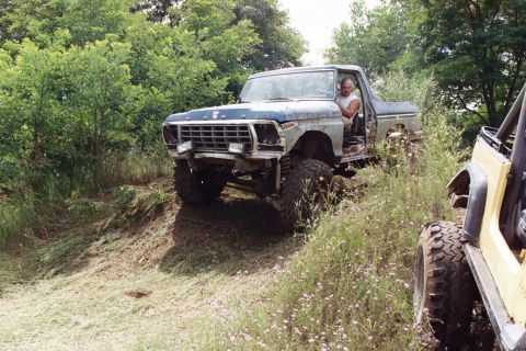 1979 Ford Bronco - A modified Ford truck navigates a grassy incline with another vehicle visible to the right.
