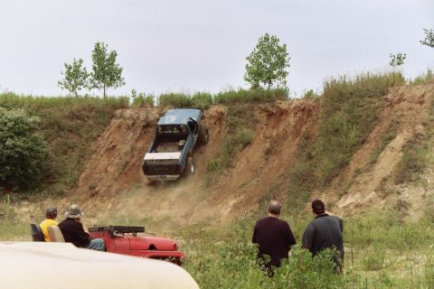 1979 Ford Bronco - A blue pickup truck navigates a steep dirt hill while onlookers watch from a red vehicle.