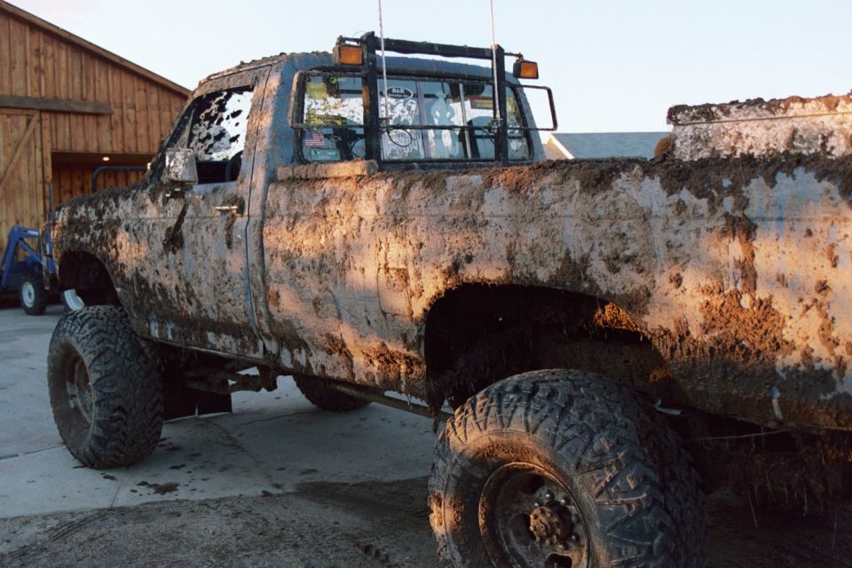 Mud-covered pickup truck, 3/4 front view, lifted suspension, aftermarket wheels, visible Supermotors logo