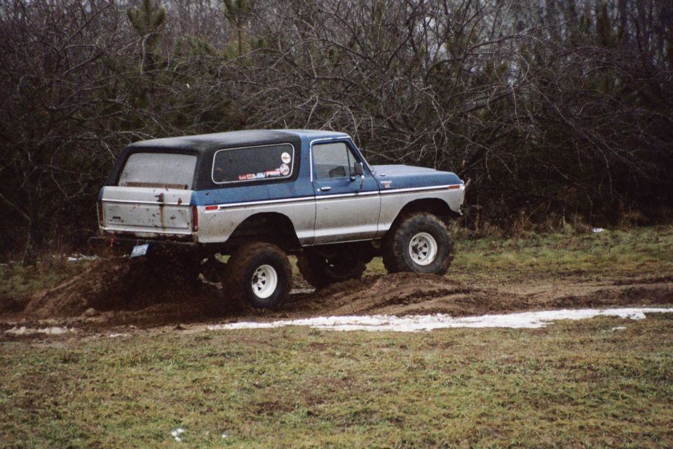 1979 Ford Bronco with lifted suspension driving through mud, blue and silver two-tone paint