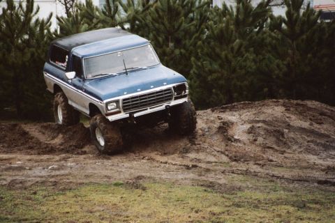 1979 Ford Bronco - This lifted Ford Bronco is navigating a muddy, uneven terrain with large tires.