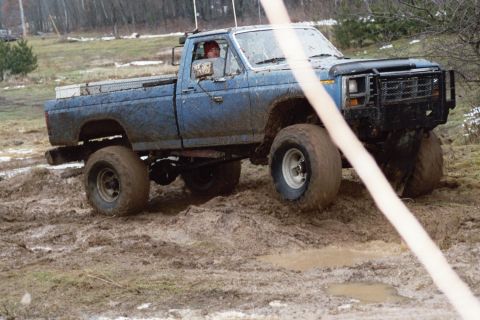 1979 Ford Bronco - A blue pickup truck navigates a muddy terrain during an outdoor event.