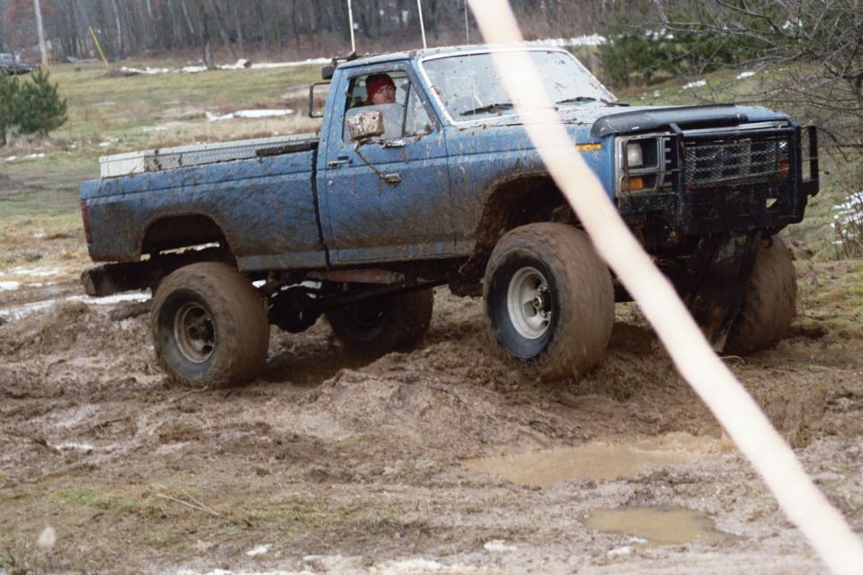 Blue pickup truck with off-road tires driving through mud