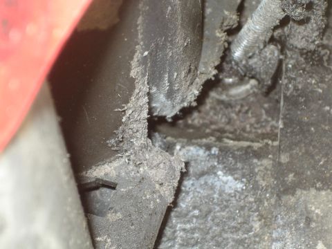 1990 Ford Bronco - close-up of a dirt-and-grease-caked black undercarriage component with a corner of red paint visible at the edge.