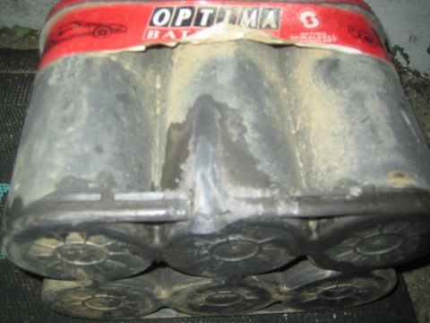 1990 Ford Bronco - worn six-cell battery with a torn red Optima label laid on its side, exposing the cylindrical spiral cells underneath.