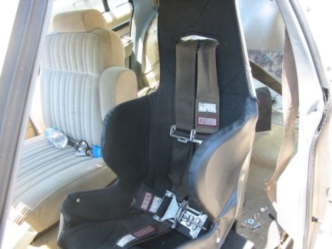 1985 Ford LTD Crown Victoria - Interior view of a car, showing a racing seat and a standard bench seat with a water bottle.