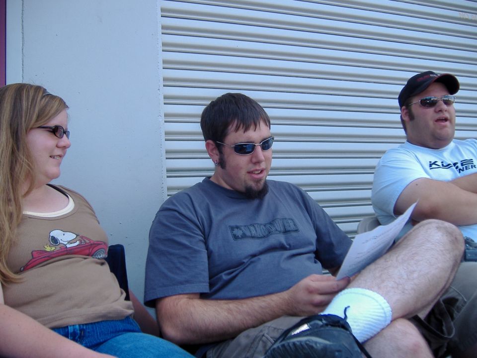 Three people sitting outdoors in front of a corrugated metal door
